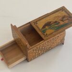 Open ornate wooden puzzle box with a painted landscape lid and hidden compartments