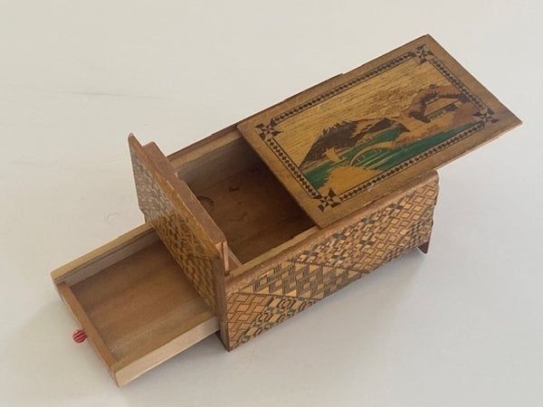 Open ornate wooden puzzle box with a painted landscape lid and hidden compartments