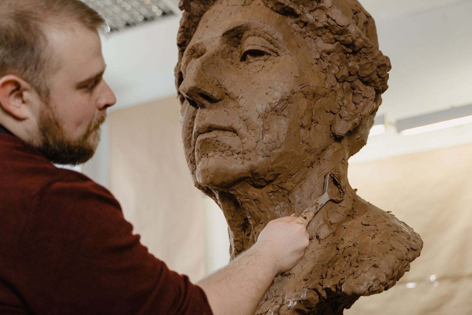 Artist sculpting a large clay humanoid creature bust